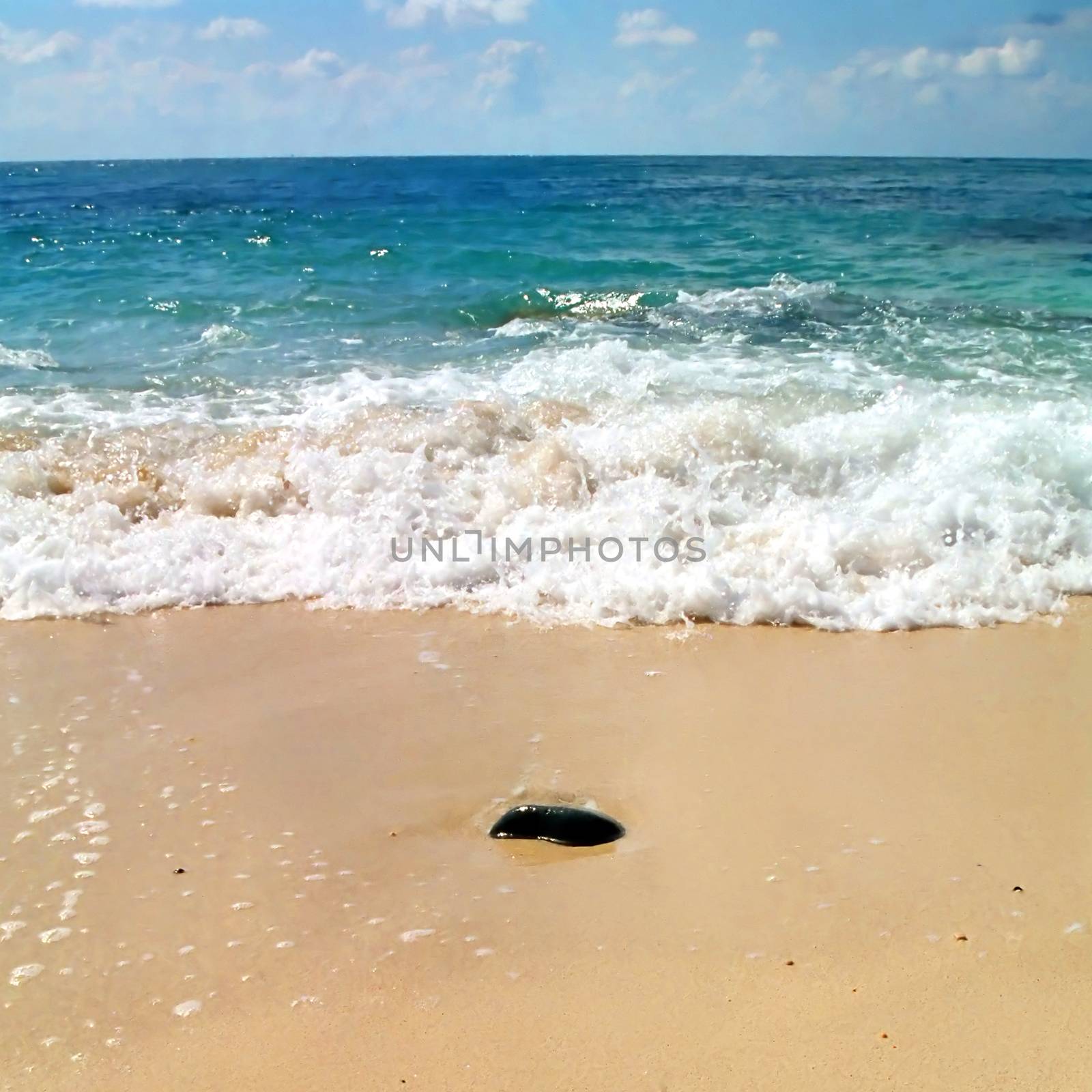 Stone in the sand and the wave behind it.