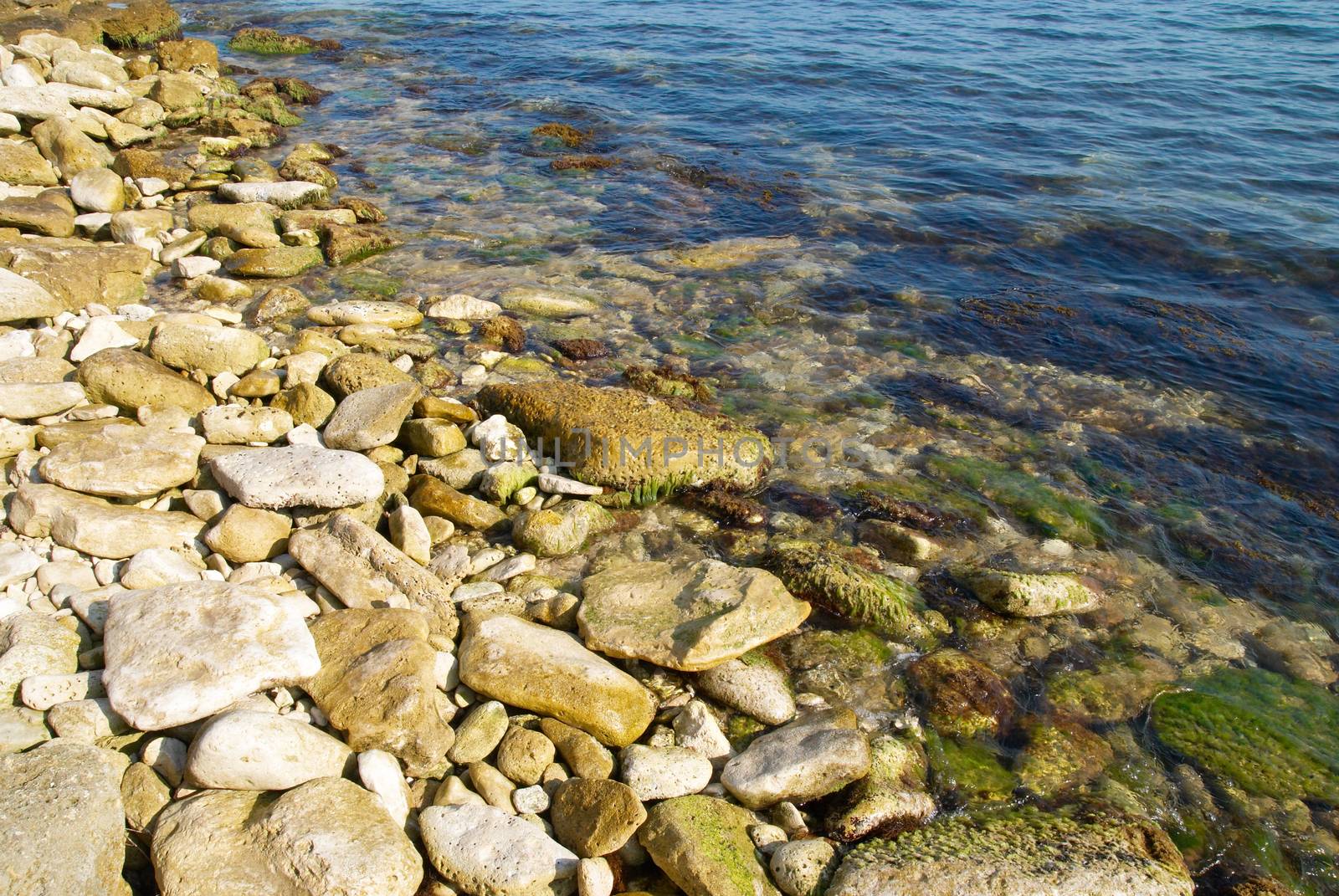 A coast with pebble and blue ocean water.