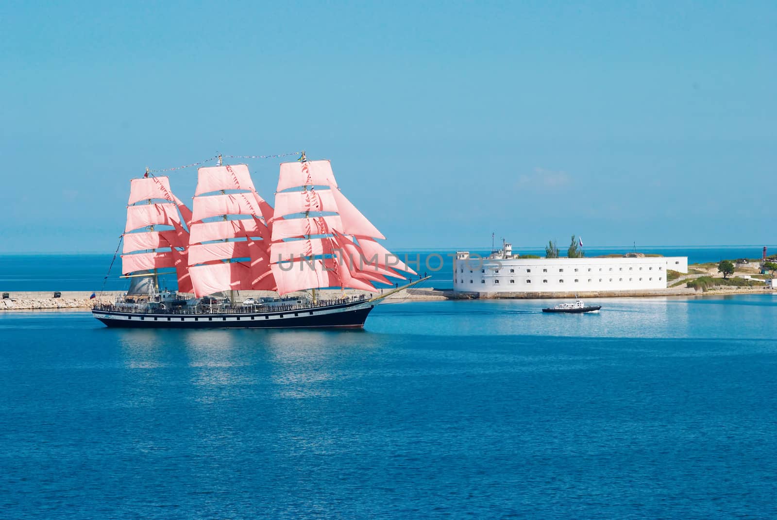 Sailing ship with red sails entering to the bay.