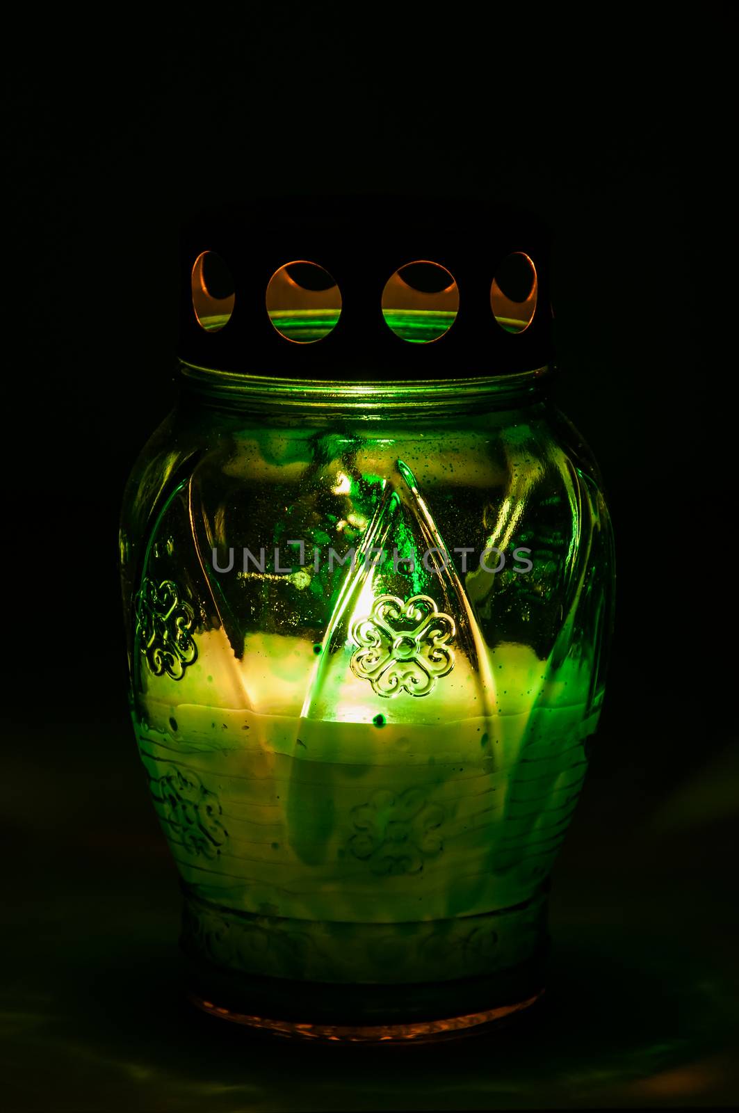 Closeup of green burning votive candle in the dark