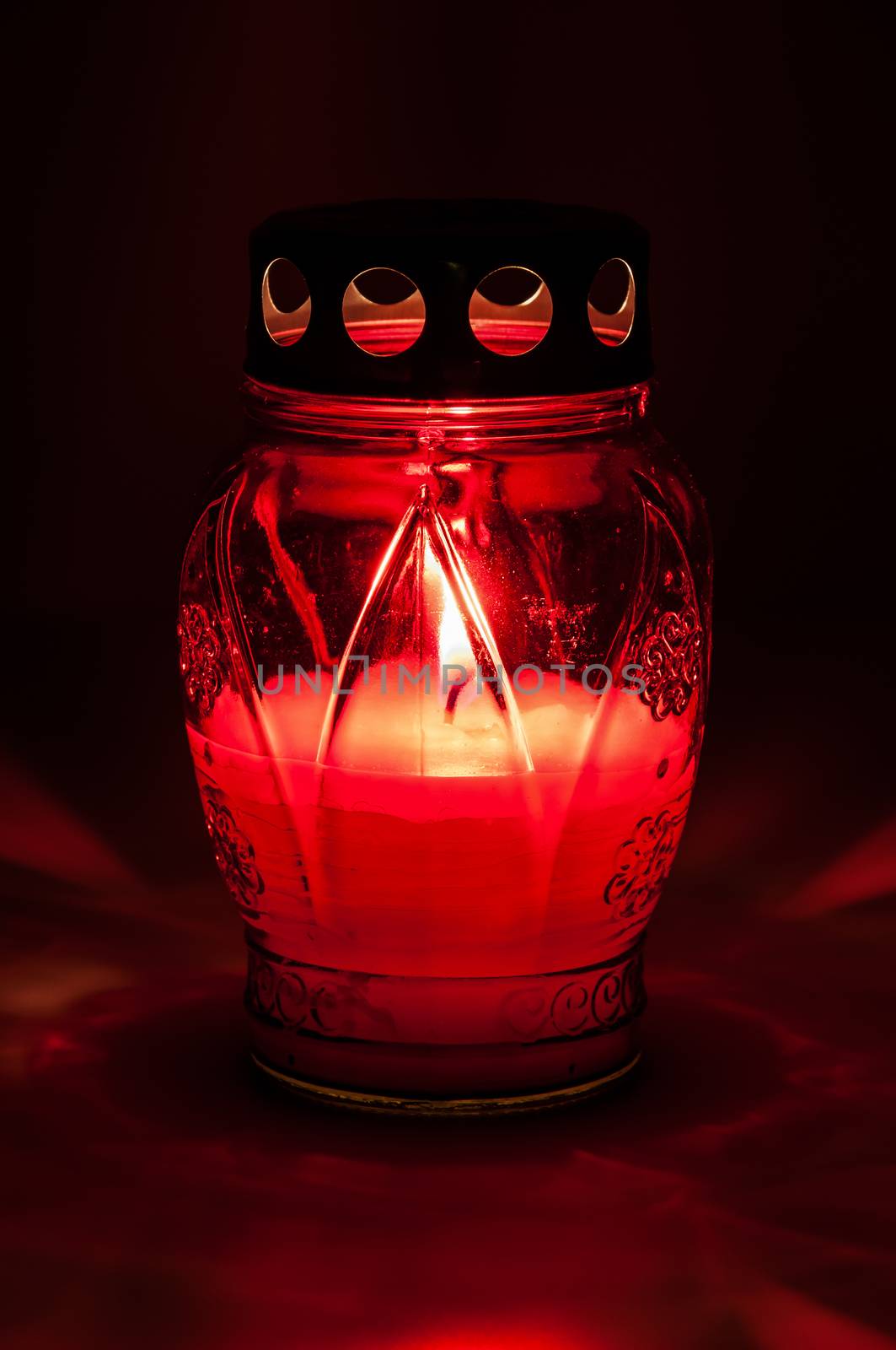 Closeup of red burning votive candle in the dark