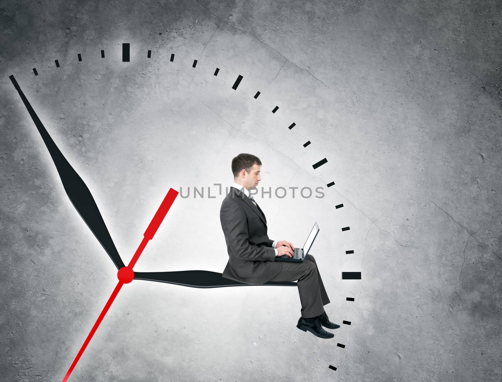 Businessman sitting on clockhand and working on computer on grey wall backgound