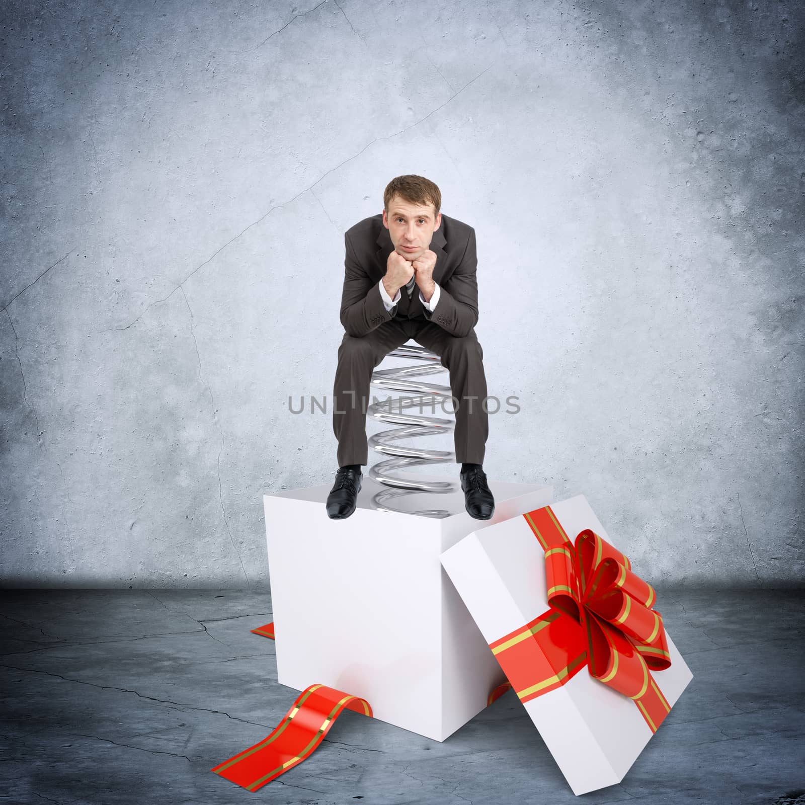 Businessman sitting on coil spring in gift box on grey wall background