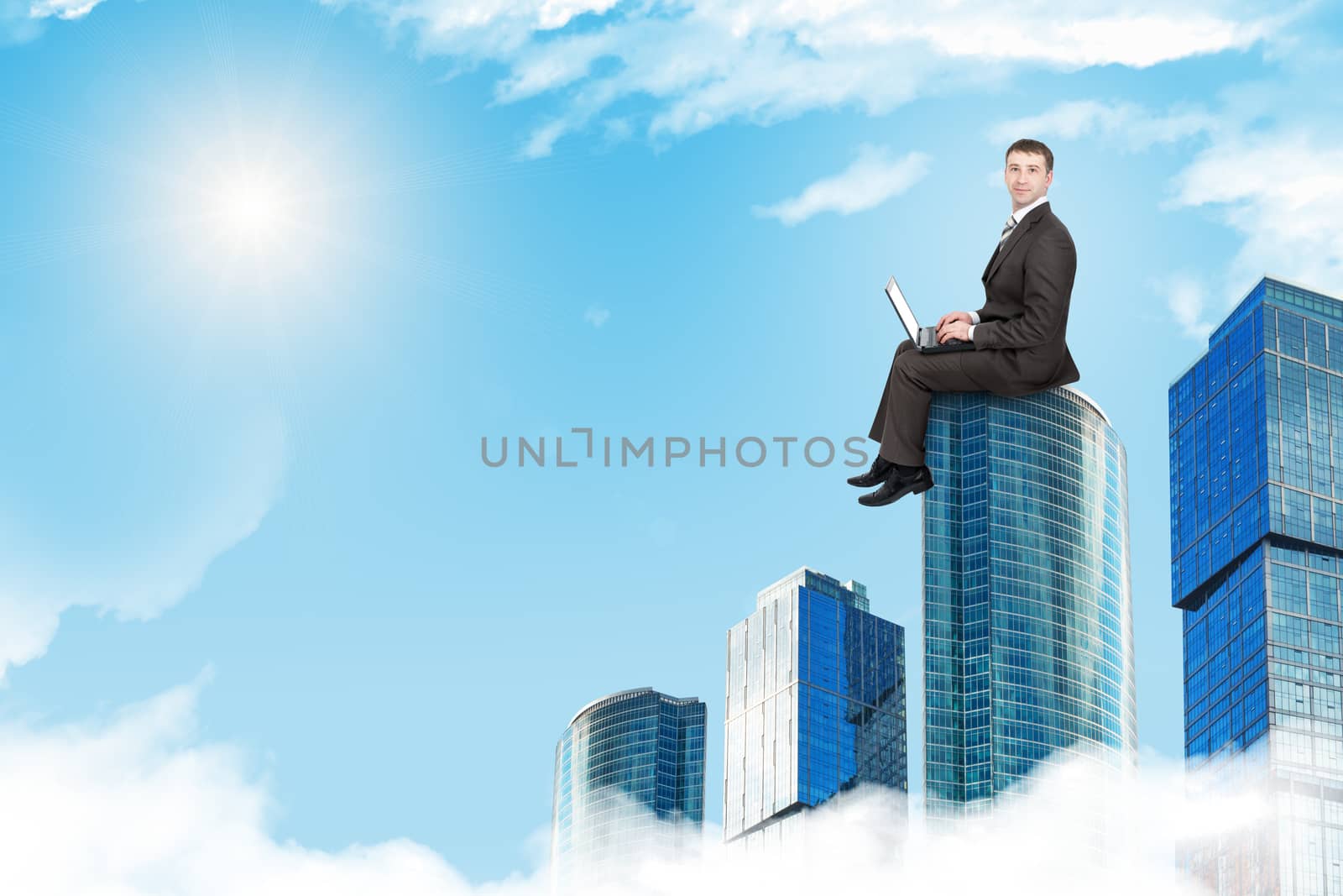Businessman working on laptop and sitting on roof and looking at camera, front view