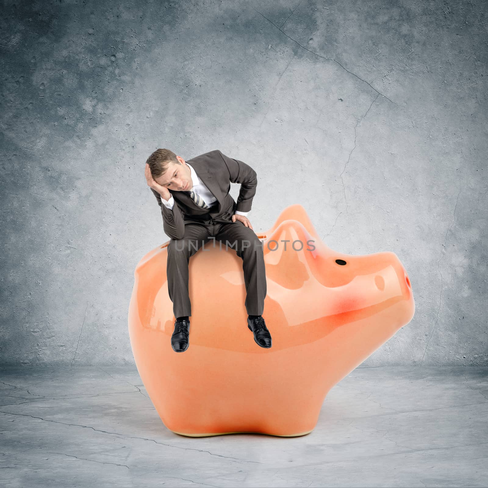 Sad businessman sitting on big piggy bank by cherezoff