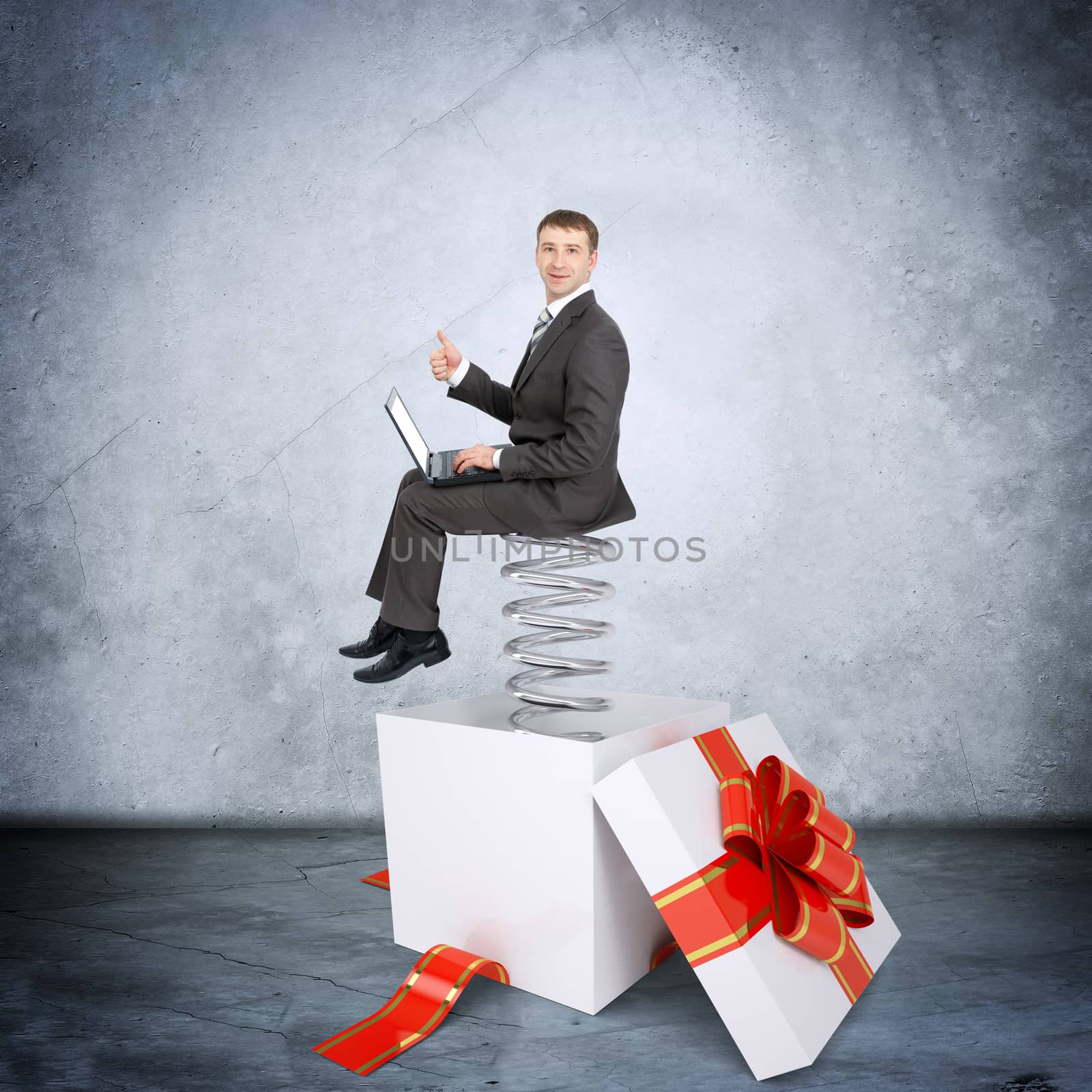Businessman working on laptop and sitting on coil spring in gift box