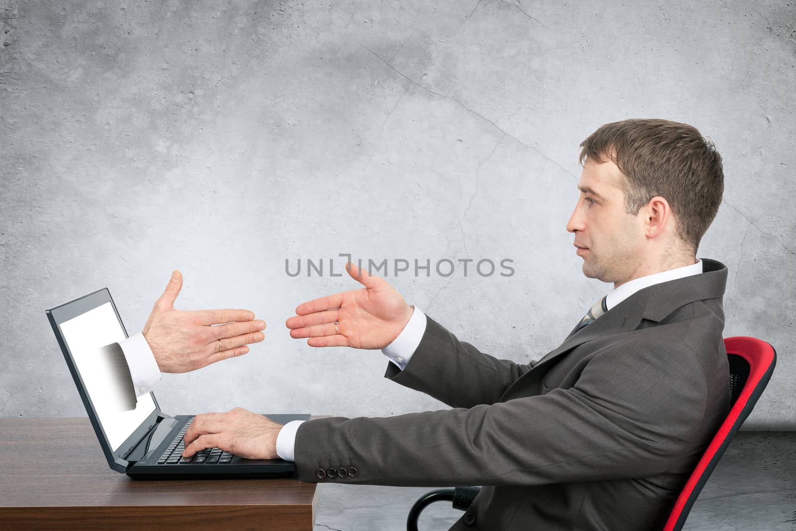 Businessman giving hand to laptop on grey wall background