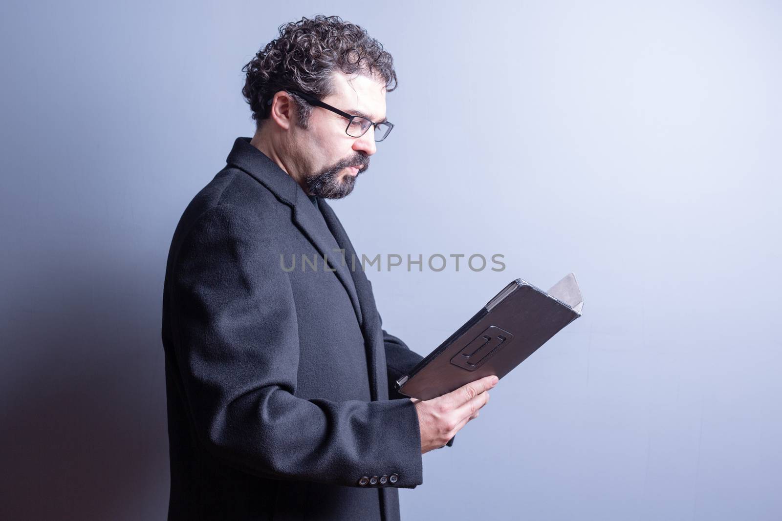 Waist Up of Business Man Wearing Suit Jacket and Eyeglasses Looking Serious While Reading Computer Tablet in Studio with Gray Background and Copy Space