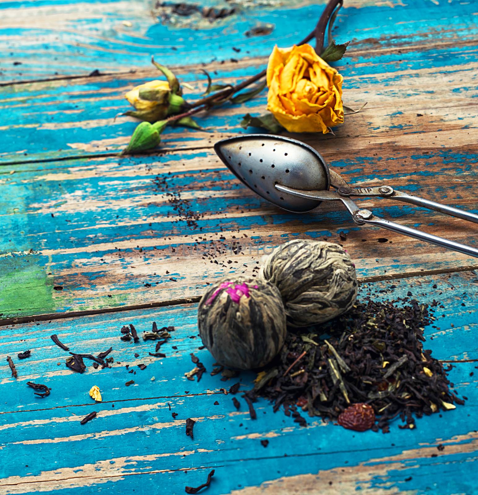 Tea leaves for brewing,tea spoon and dried yellow rose.The image is tinted in vintage style