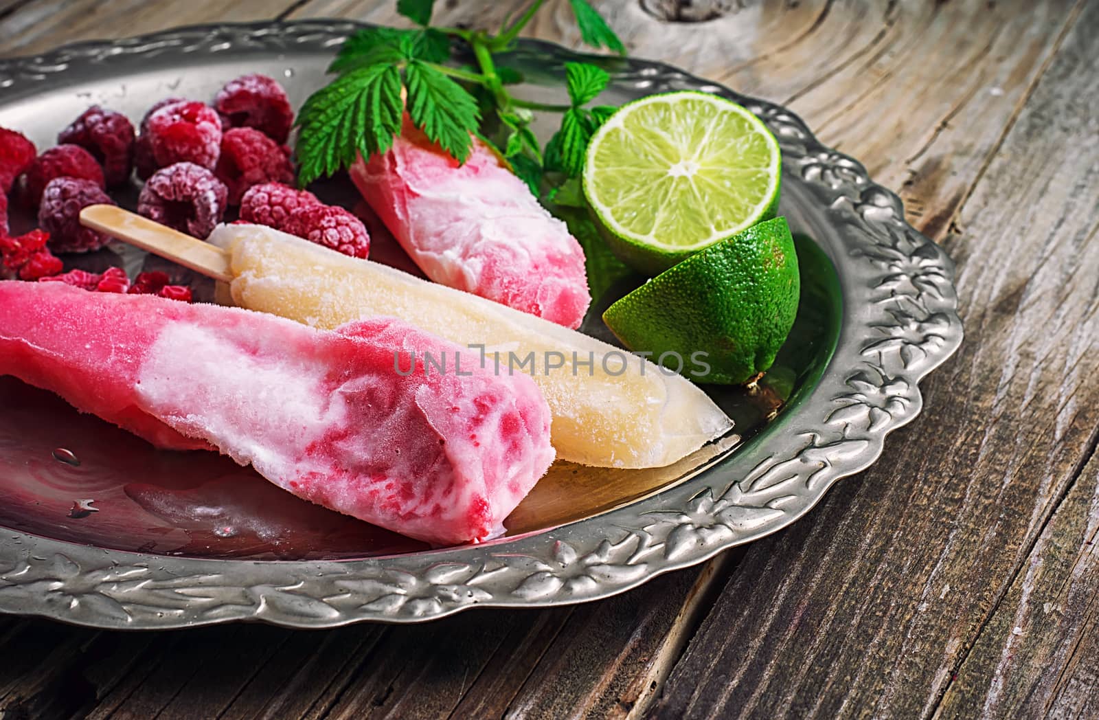 Popsicles served with raspberries and lime on a metal tray.Selective focus