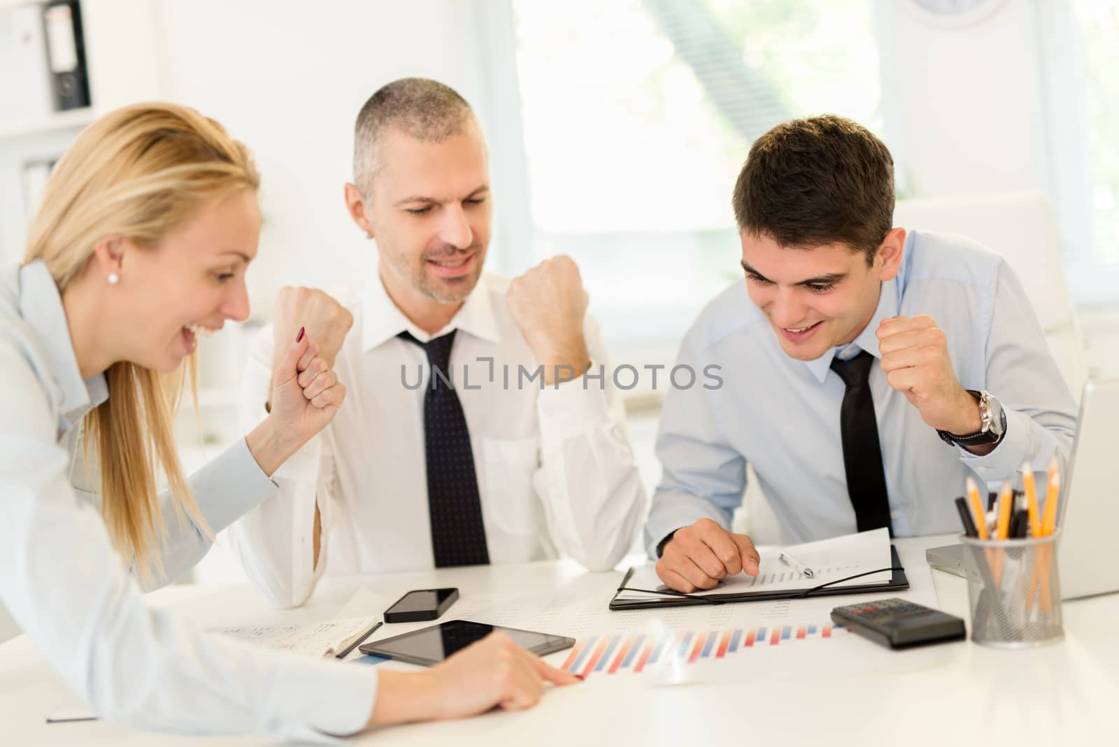 Successful young business people having a meeting in the office. Three business people looking at document and discussing, with raised arms celebrating success.