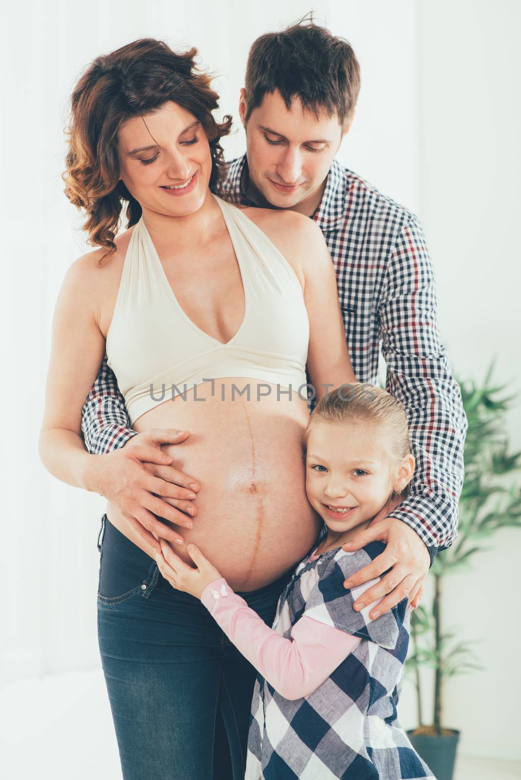Beautiful young family cuddling the woman's pregnant belly. 