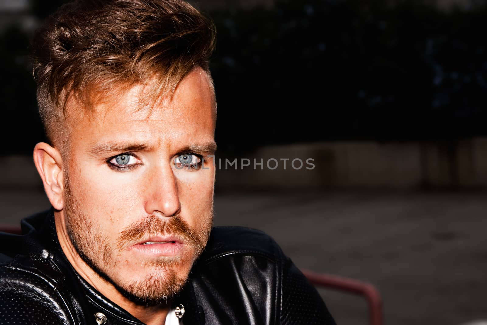 Portrait of a fashionable young man with blue eyes, stylish haircut and posing with a black jacket. Close up. Copy-space. Horizontal image.