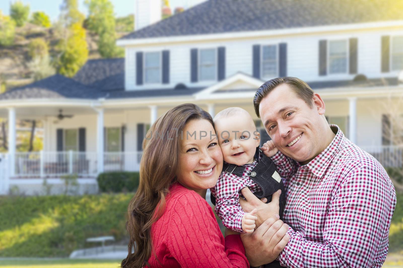Happy Young Family With Baby Outdoors In Front of Beautiful Custom Home.