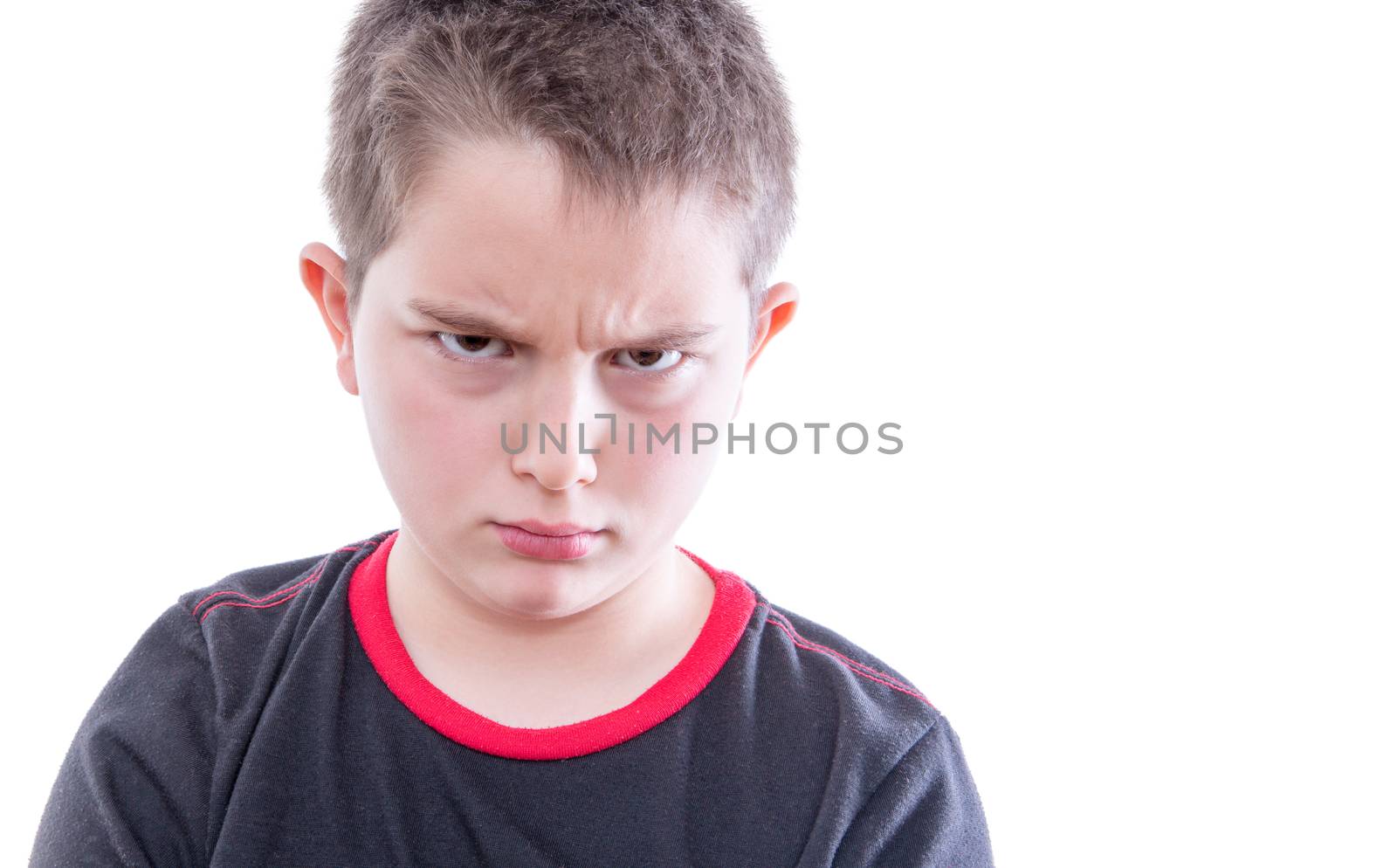 Head and Shoulders Close Up Portrait of Young Tween Boy Wearing Black and Red T-Shirt Frowning with Furrowed Brow at Camera in Studio with White Background and Copy Space