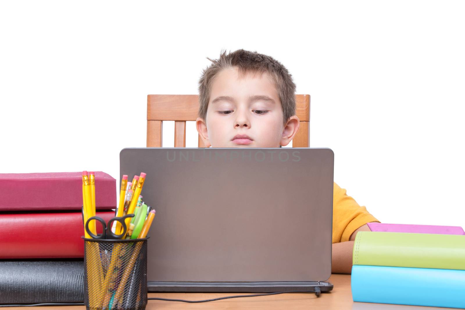 Young Boy Looking Down at Laptop Computer Screen While Studying at Desk with Pencil Holder and Supplies and Surrounded by Colorful Books and Binders, in Room with White Background and Copy Space