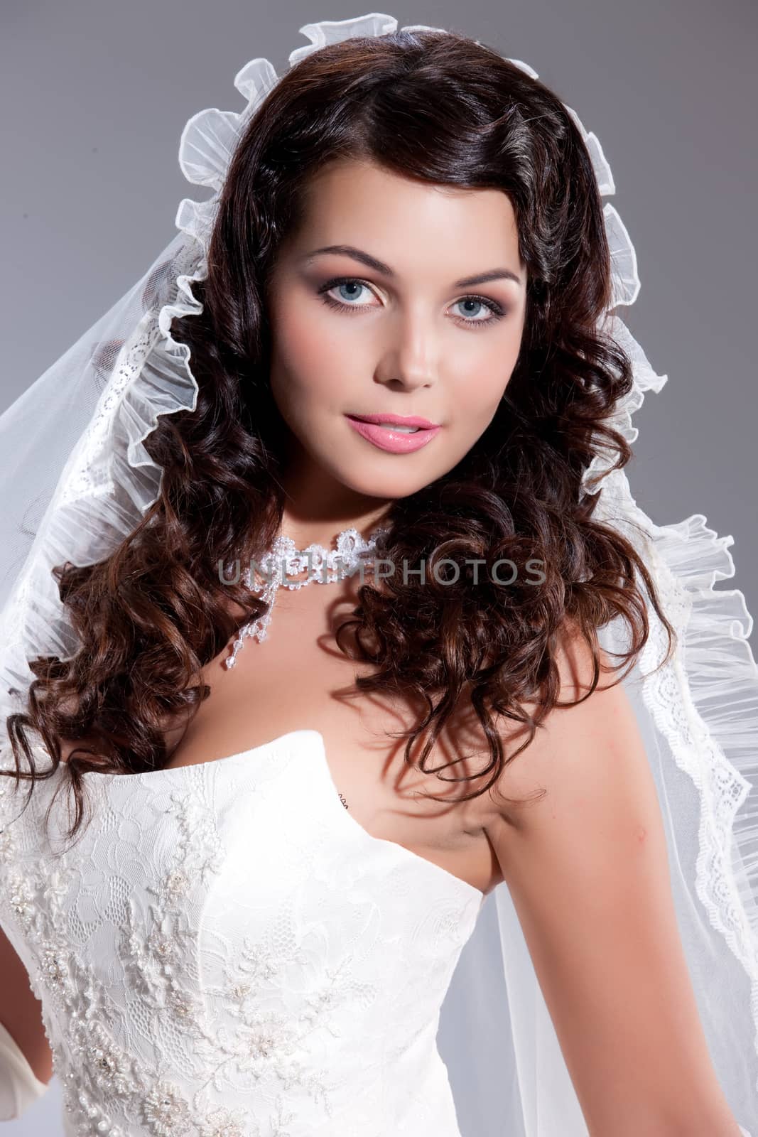 Young beautiful brunette in fashionable wedding dress on isolated studio background