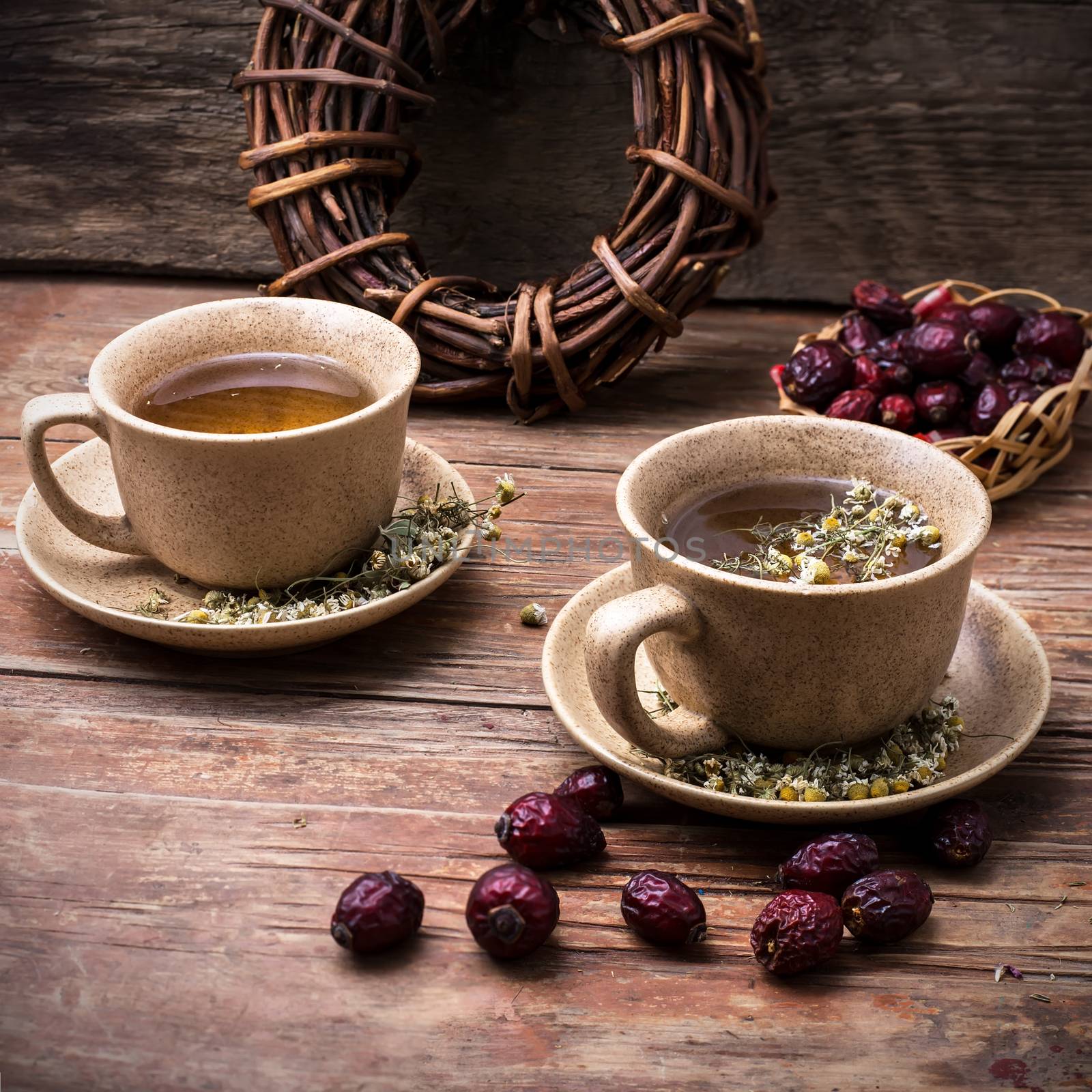 Two ceramic cups brewed tea with rosehip and chamomile amid bundles of licorice root