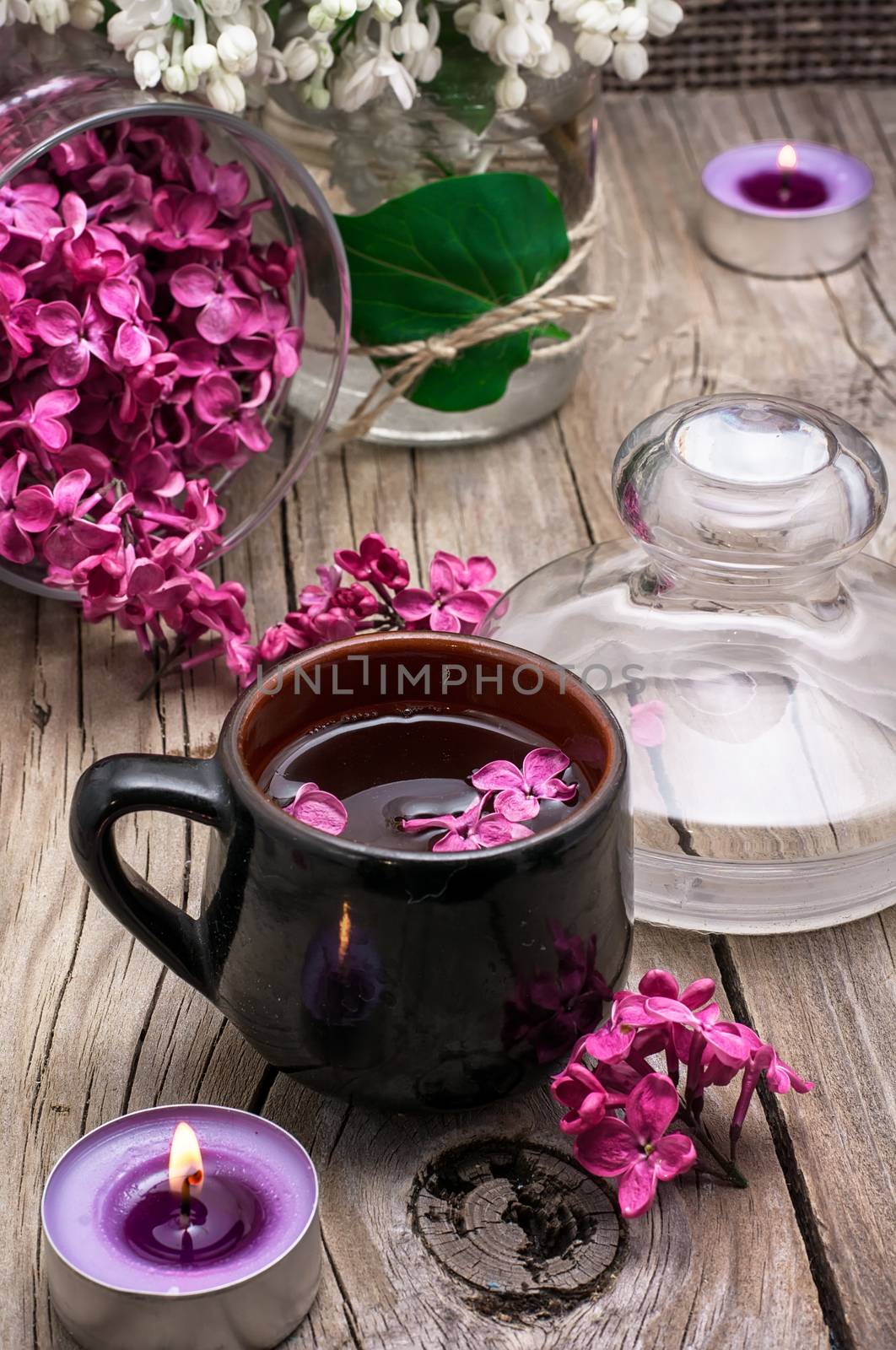 fragrant spring flower tea on the background of burning candles and lilac bouquet