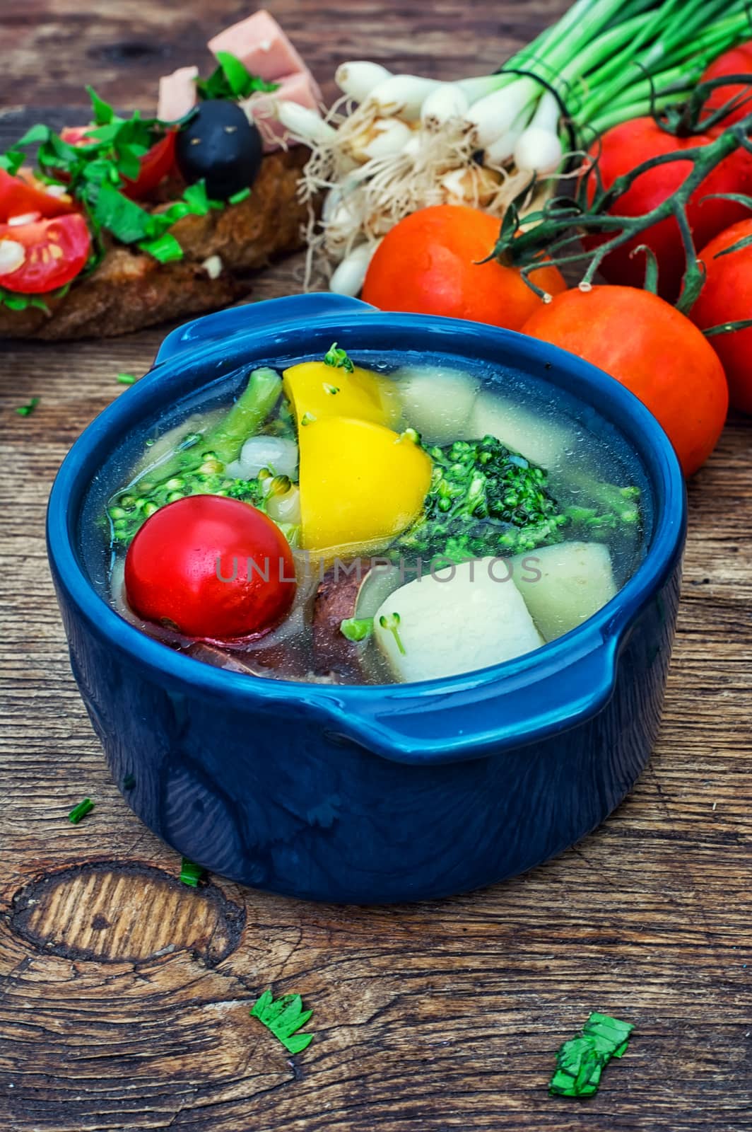traditional soup of fresh vegetables in blue pot on wooden background