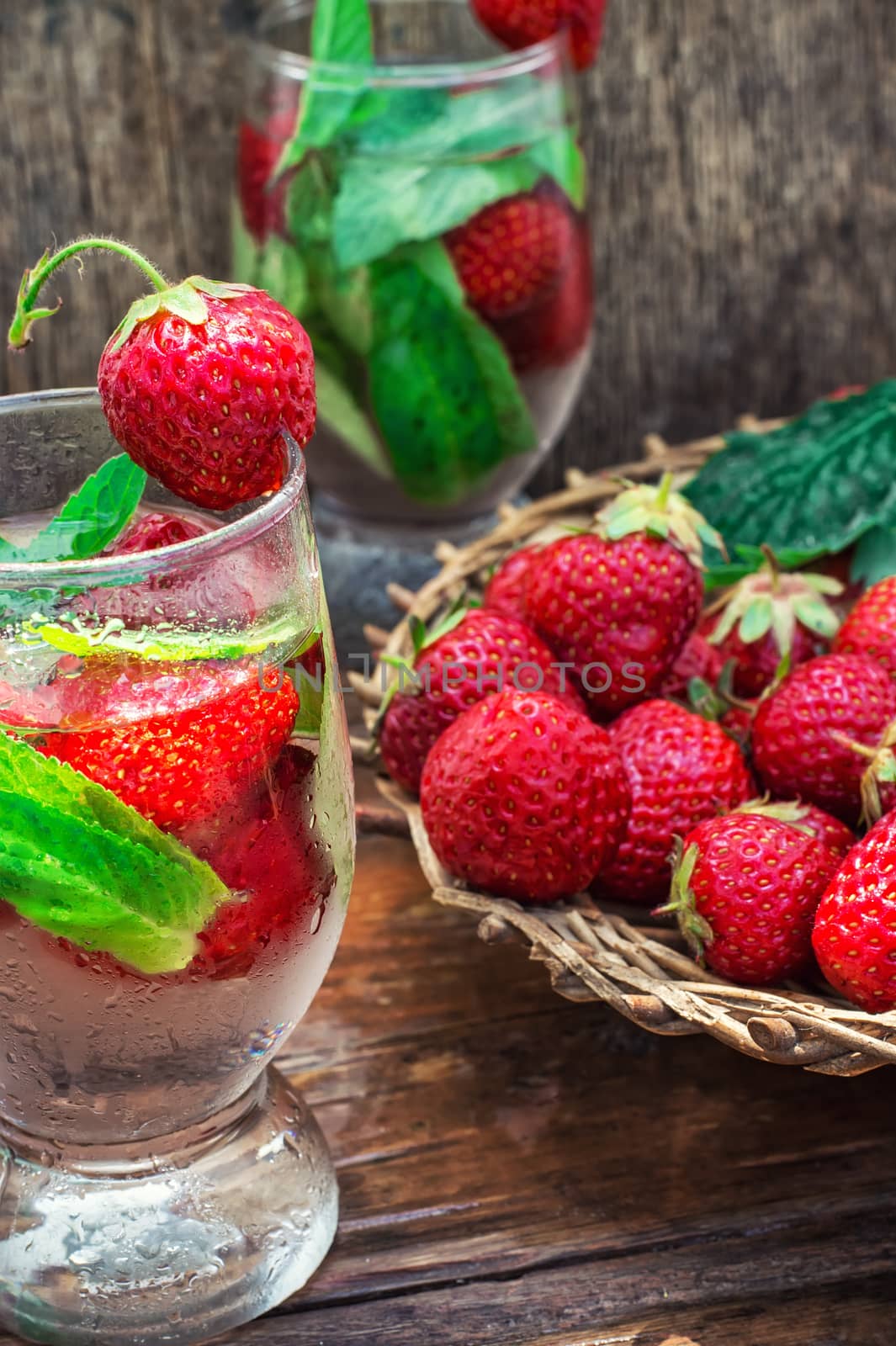 glass with drink of strawberries and mint on the background of the basket full berries.Selective focus.Photo tinted
