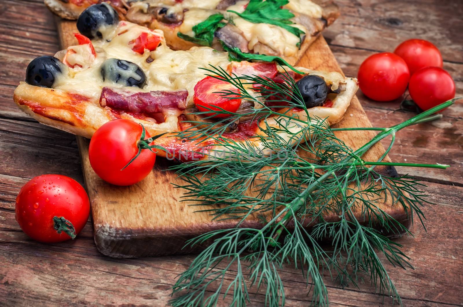 hunk of delicious meat pizza with bacon and olives on the background of the vegetables.The image is tinted