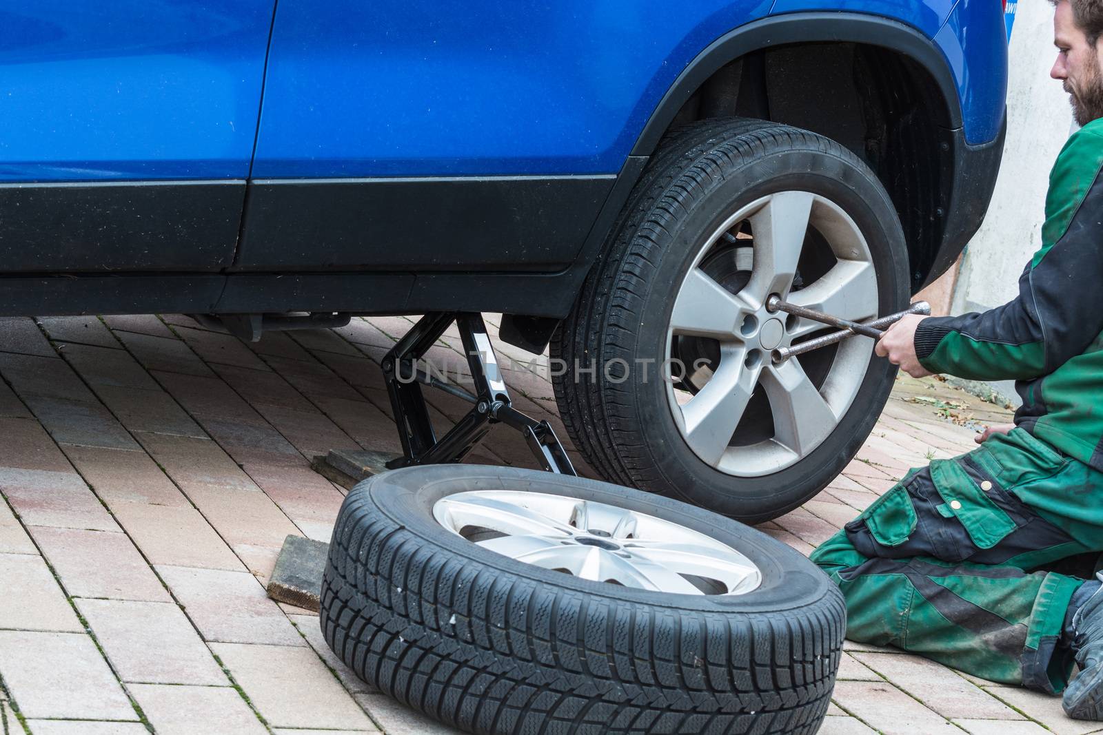 Young man  exchanging the car tires. From summer tires on winter tires on his car.