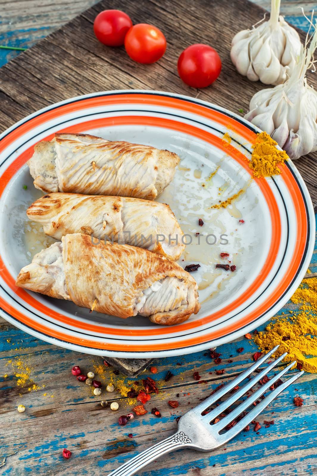 Turkey sausages roasted on round plate on wooden surface with tomatoes and spices.