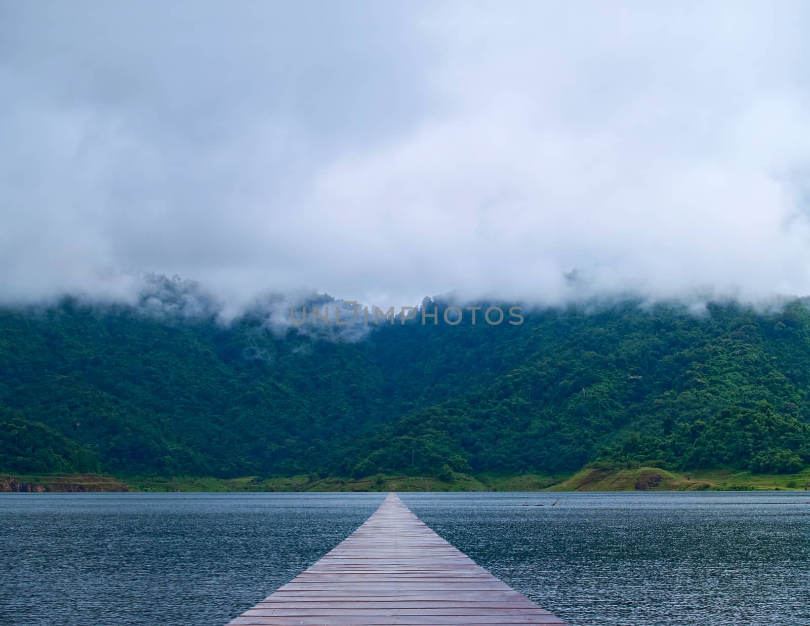 Boardwalk over lake lead to misty mountain and forest in morning