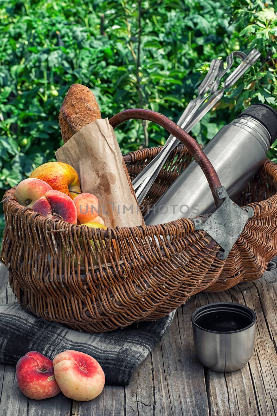 Straw basket with bread loaf,fruit and thermos for picnic on the background lawn .Photo tinted.