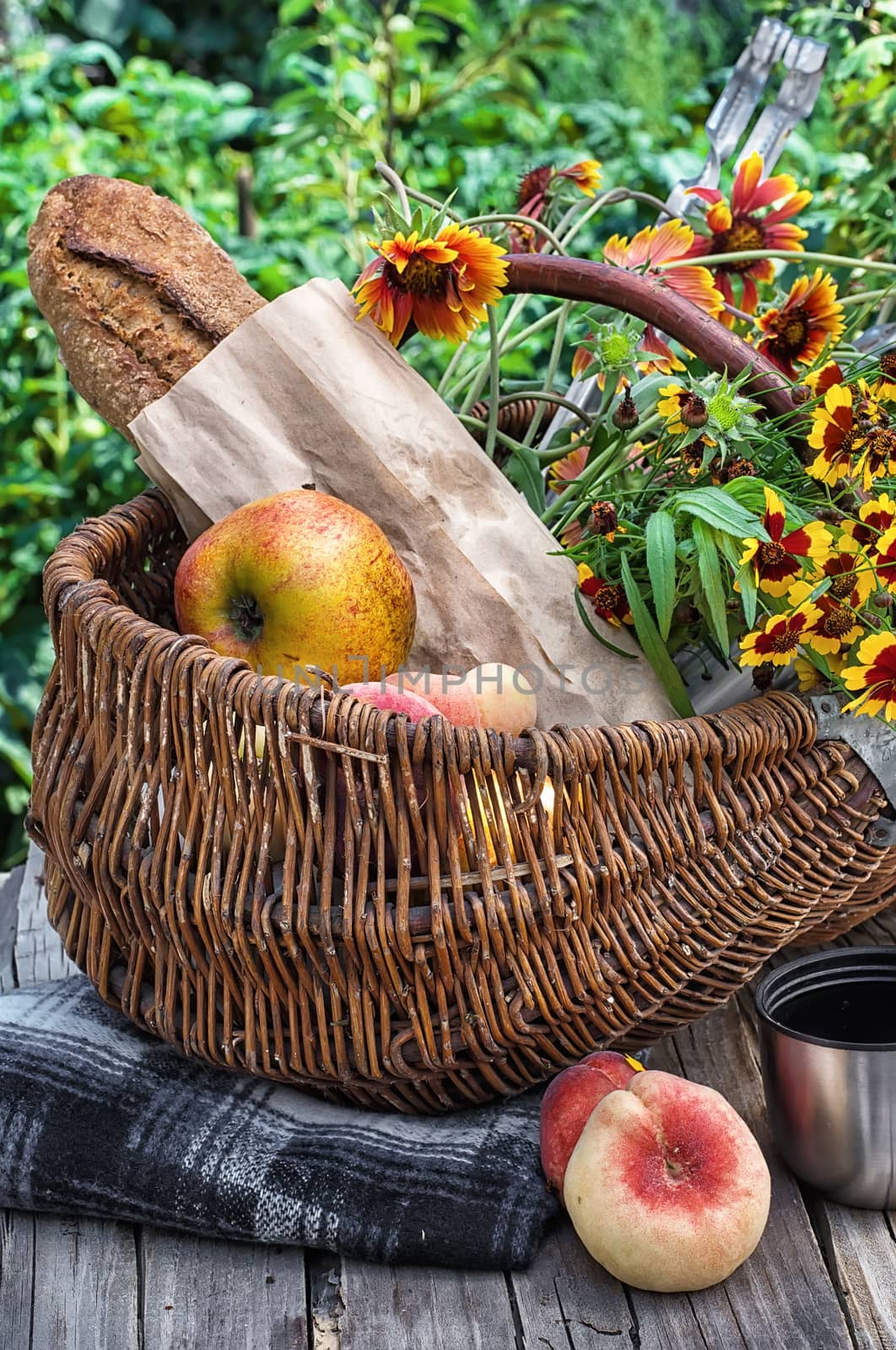 Straw basket with bread loaf,fruit and thermos for picnic on the background lawn .Photo tinted.