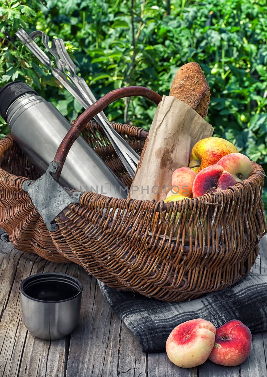 Straw basket with bread loaf,fruit and thermos for picnic on the background lawn .Photo tinted.