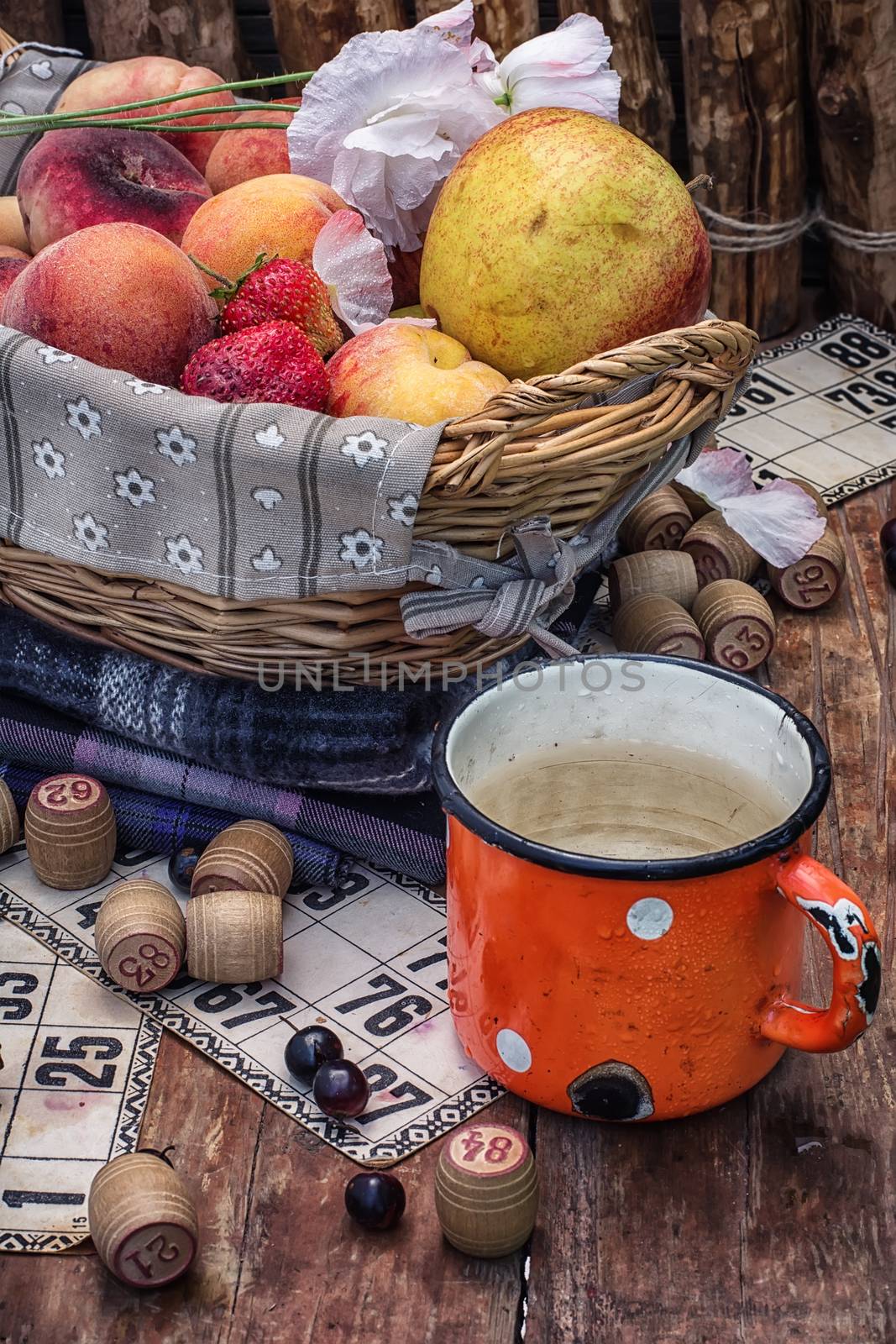 composition of the enamel cup with water on the background  fruit basket and Lotto games for picnic
