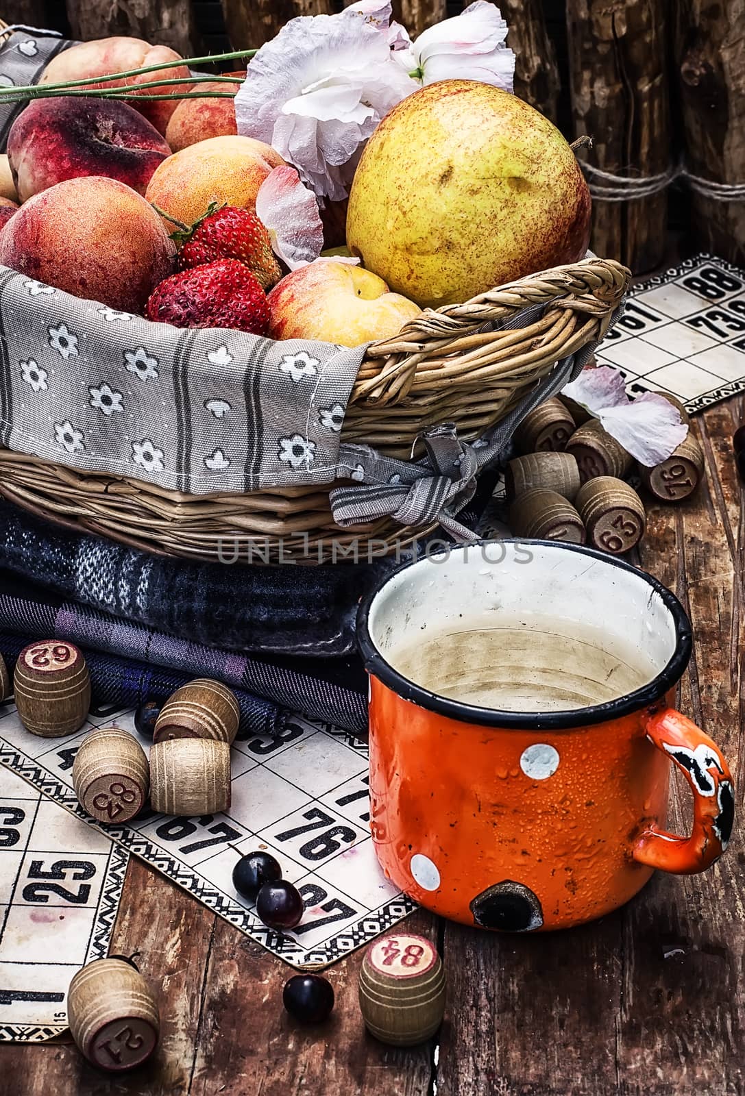 composition of the enamel cup with water on the background  fruit basket and Lotto games for picnic.Photo tinted.