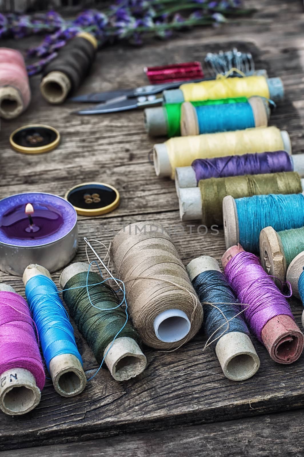 spools of thread on the old wooden background decorated with branches blossoming lavender.Selective focus