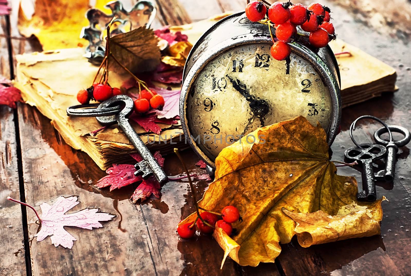 Od clock book and the keys on the wet table strewn with autumn leaves.Photo tinted.