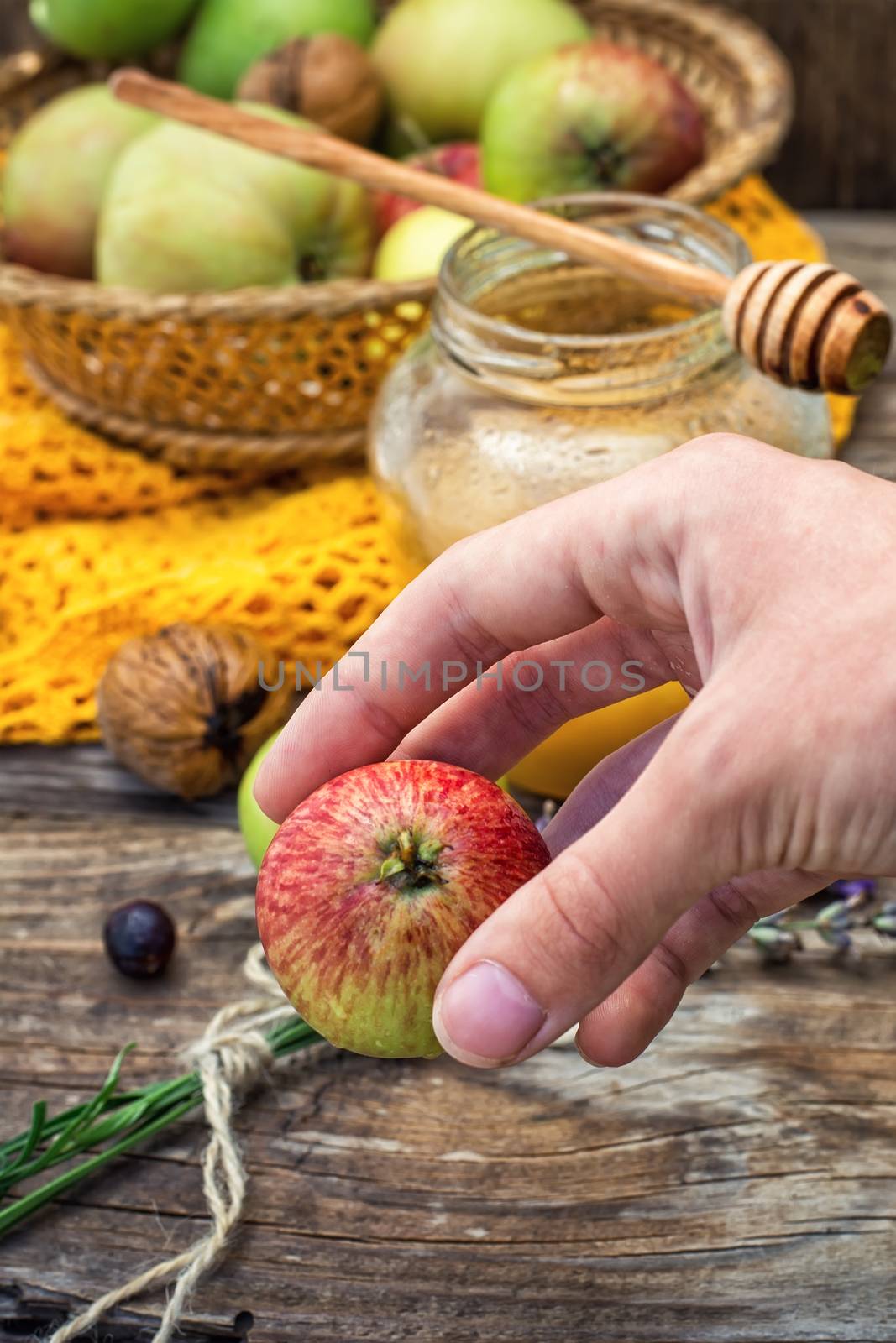 apple in hand on the background of the glass jar with fragrant honey and fruits