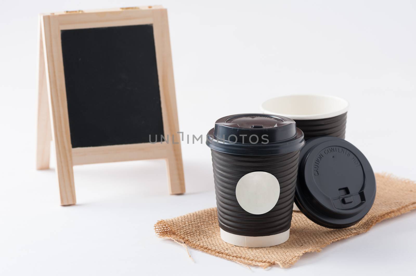 Take away paper coffee cup with white sticker label for logo, text or message and small A-frame black board in blurry background