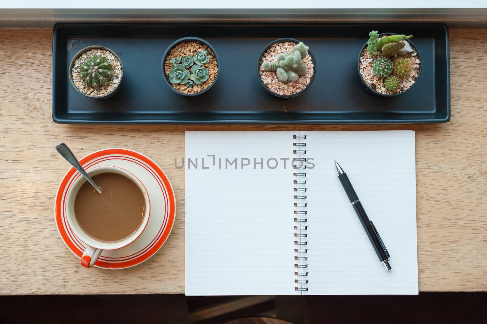 Top view of coffee cup and opened notebook with pen on wood bar beside window at coffee shop in morning time