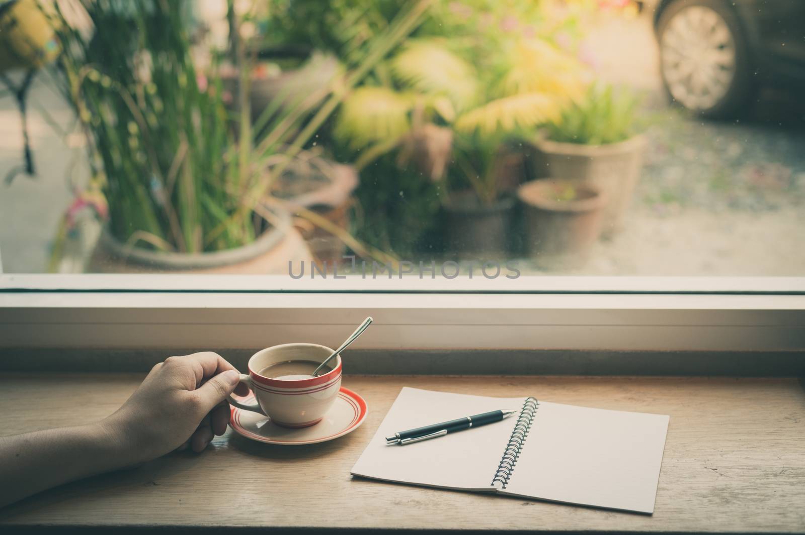 Male hand holding coffee cup on wood bar beside window at cafe in morning time with film filter effect