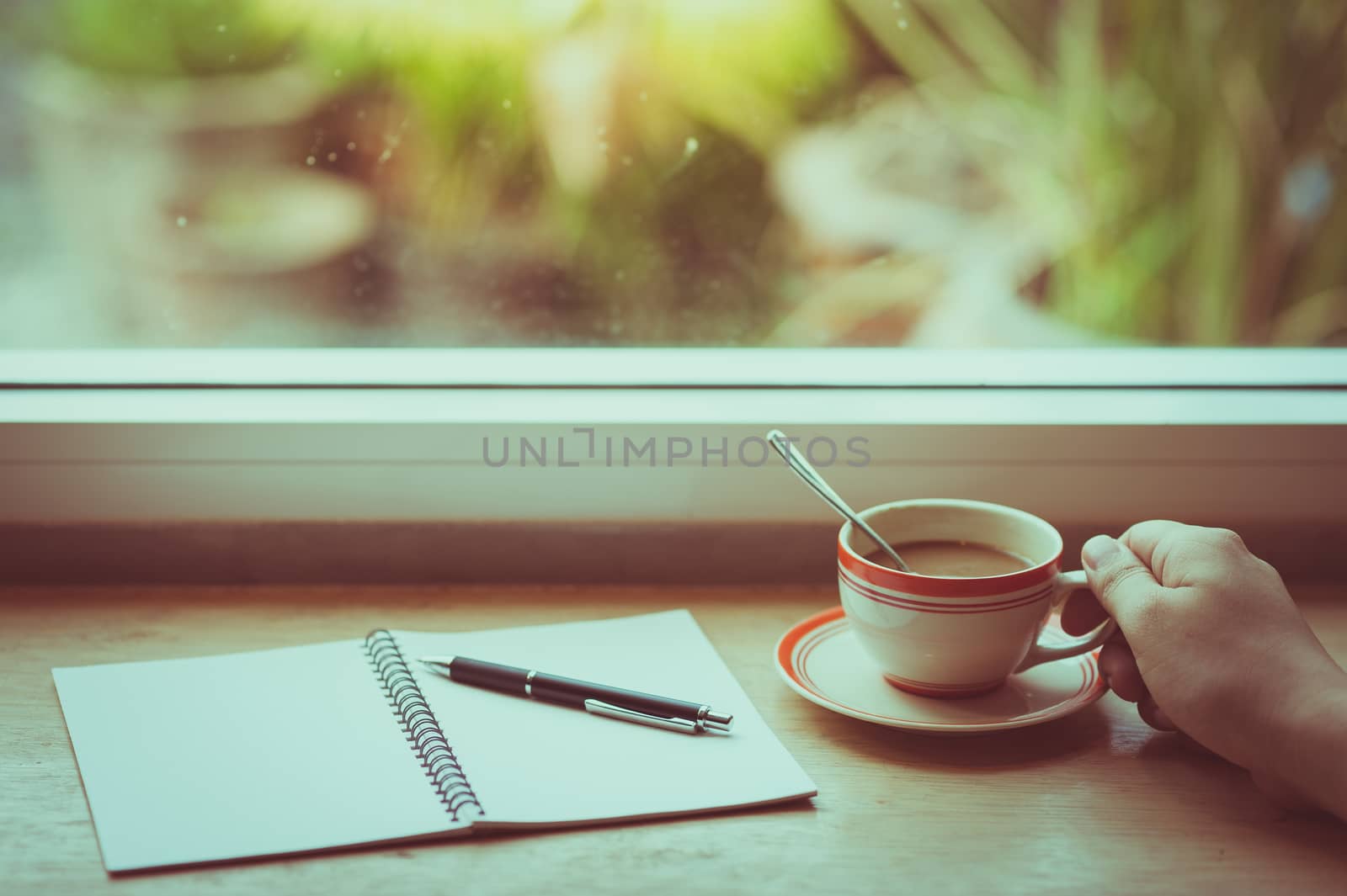 Male right hand holding coffee cup on wood bar beside window at cafe in morning time with vintage filter effect