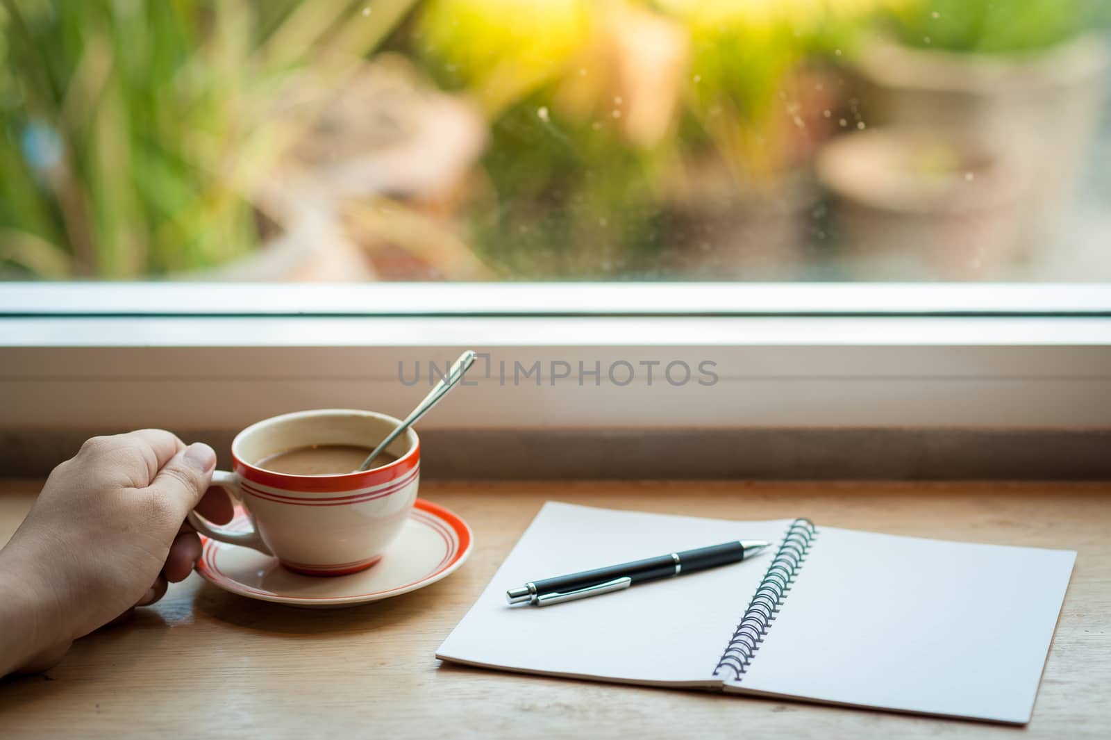 Male left hand holding coffee cup on wood bar beside window at cafe in morning time