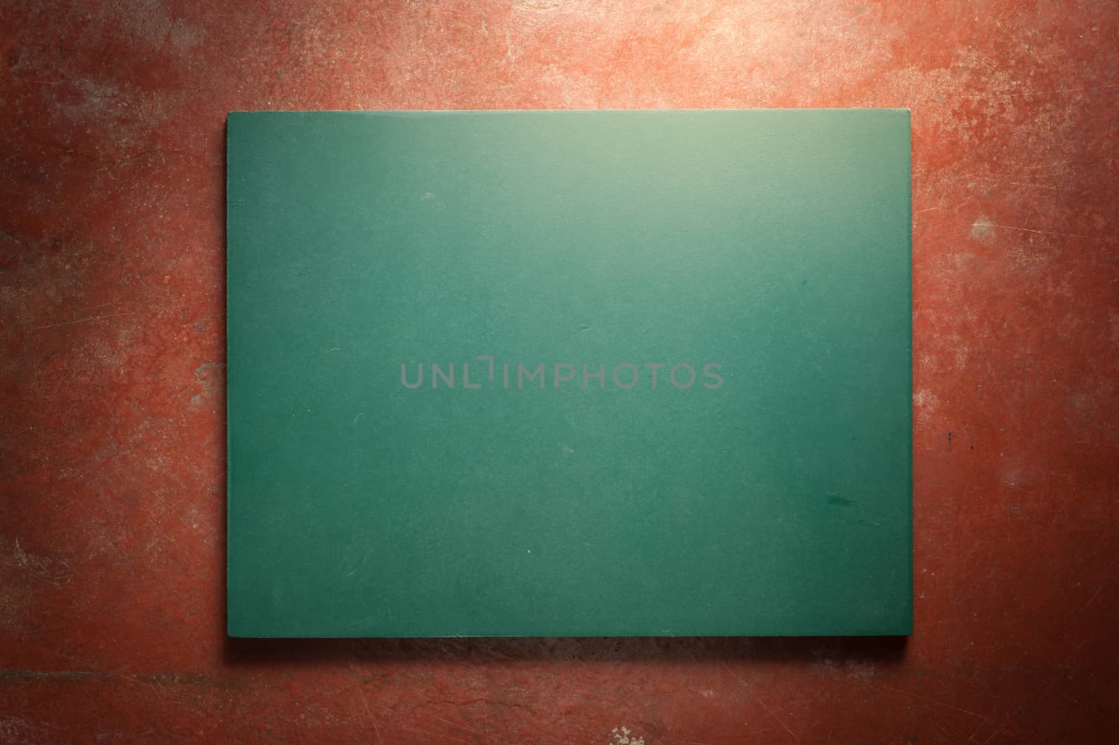 Small black board in green color with blank space for text or message on veteran red cement background with low key scene