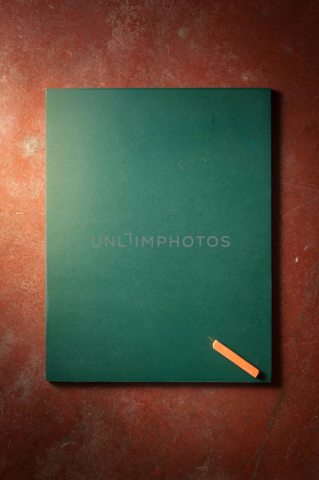 Small black board in green color with blank space for text or message on veteran red cement background with low key scene