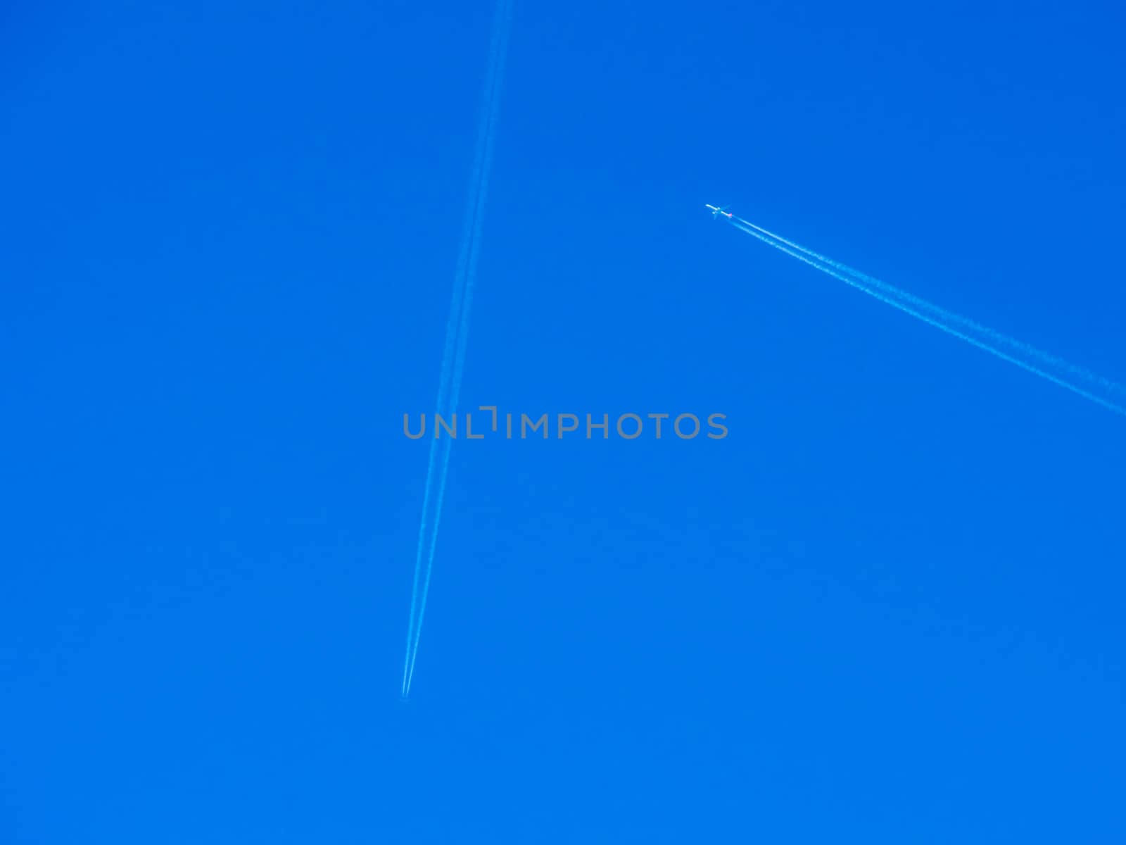 Aeroplanes flying through clear blue sky with vapour trails