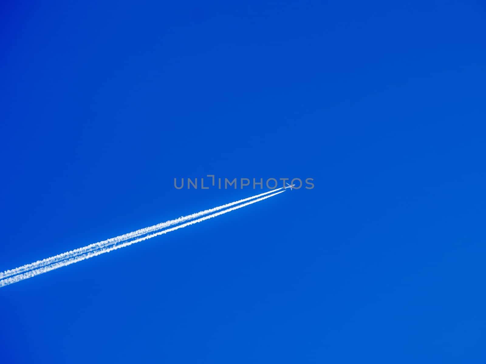 Aeroplane flying through clear blue sky with vapour trails