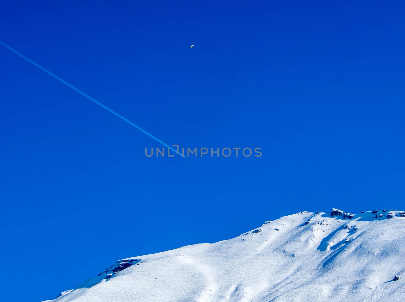 Aeroplane flying above a mountain with vapour trails and para-sailer