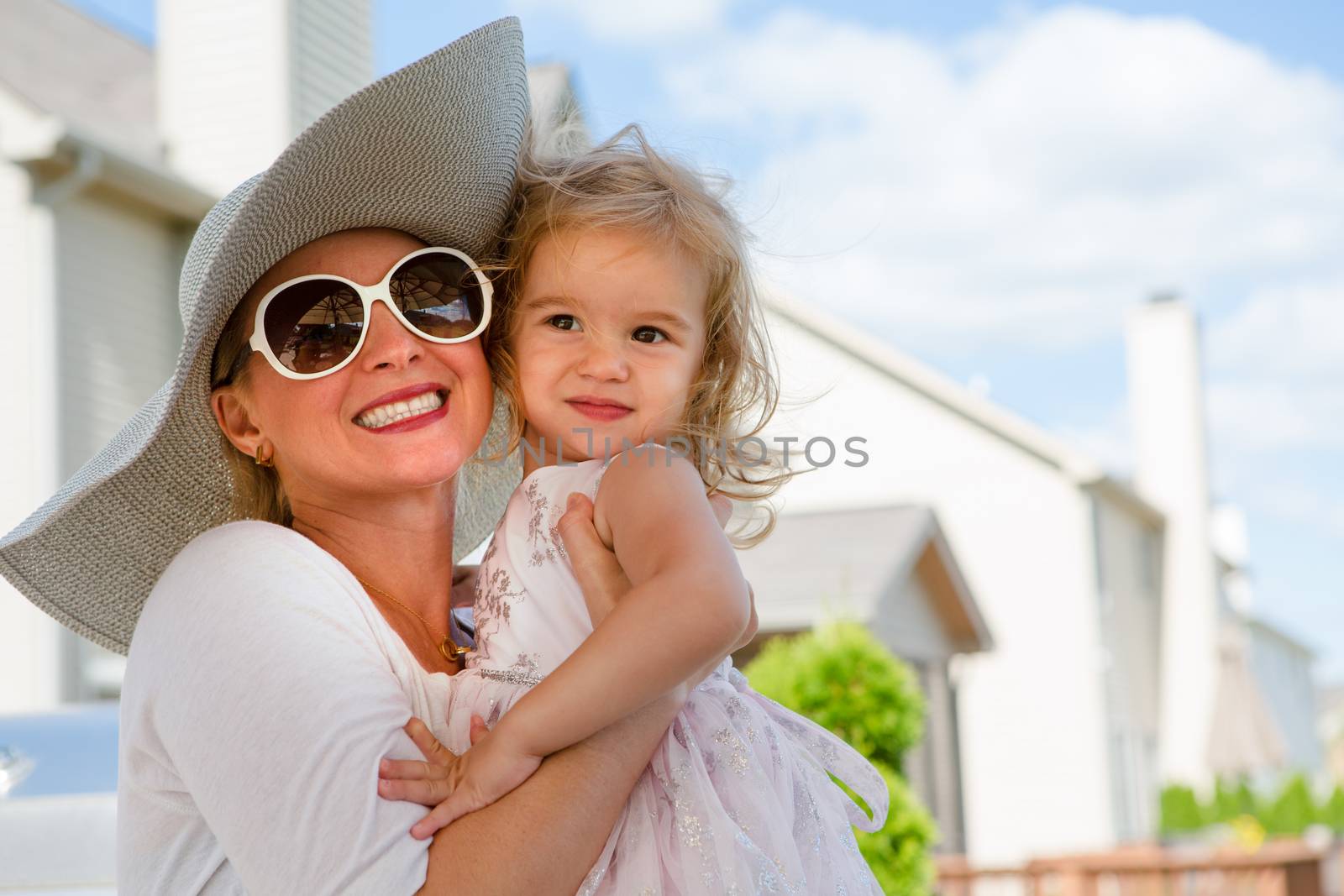 Waist Up Portrait of Woman Wearing Sun Hat and Sunglasses Hugging Young Blond Girl Outdoors in Backyard on Sunny Summer Day