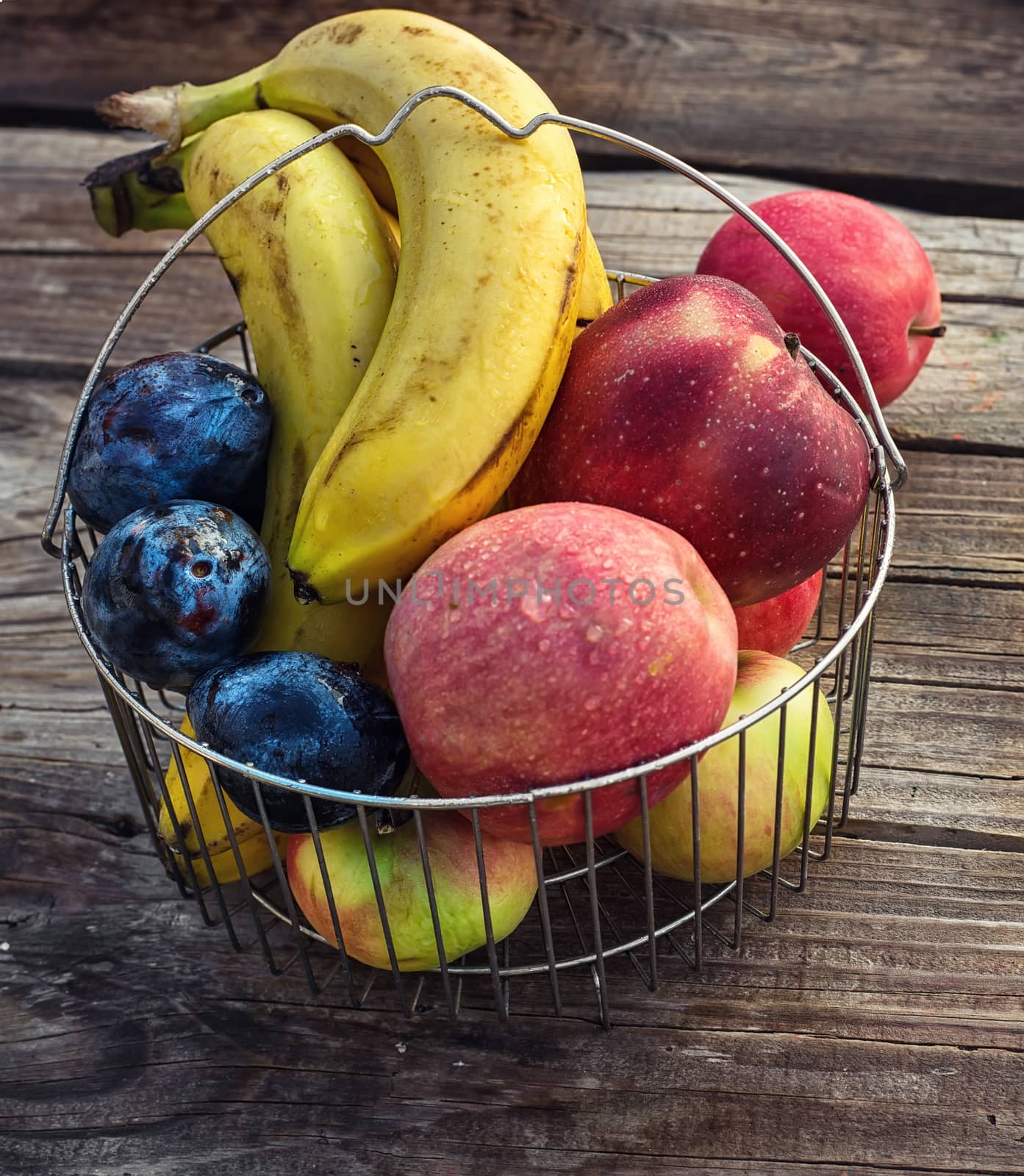 Ripe apples,bananas and plums in metal basket on wooden background