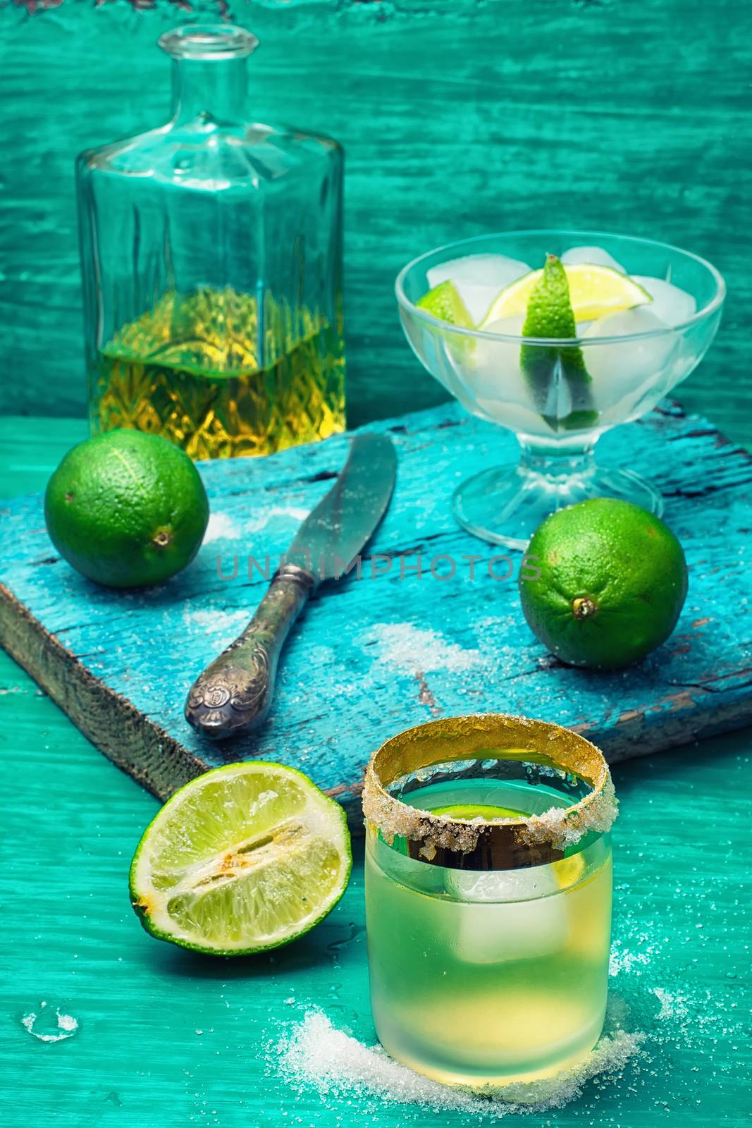 Glass with alcohol and fruits of lime and the bowl with ice  on wooden background